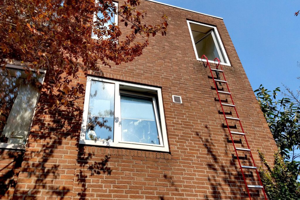 De buitenkant van een nieuwbouwhuis met een raam waar een brandladder uit hangt