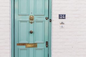 Een turquoise blauwe deur met daarnaast een deurbel en huisnummer