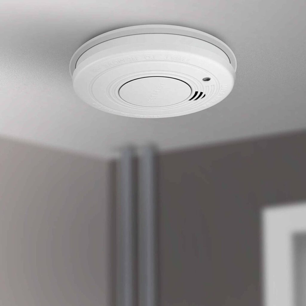 Een plafond met een rookalarm en een grijze muur
